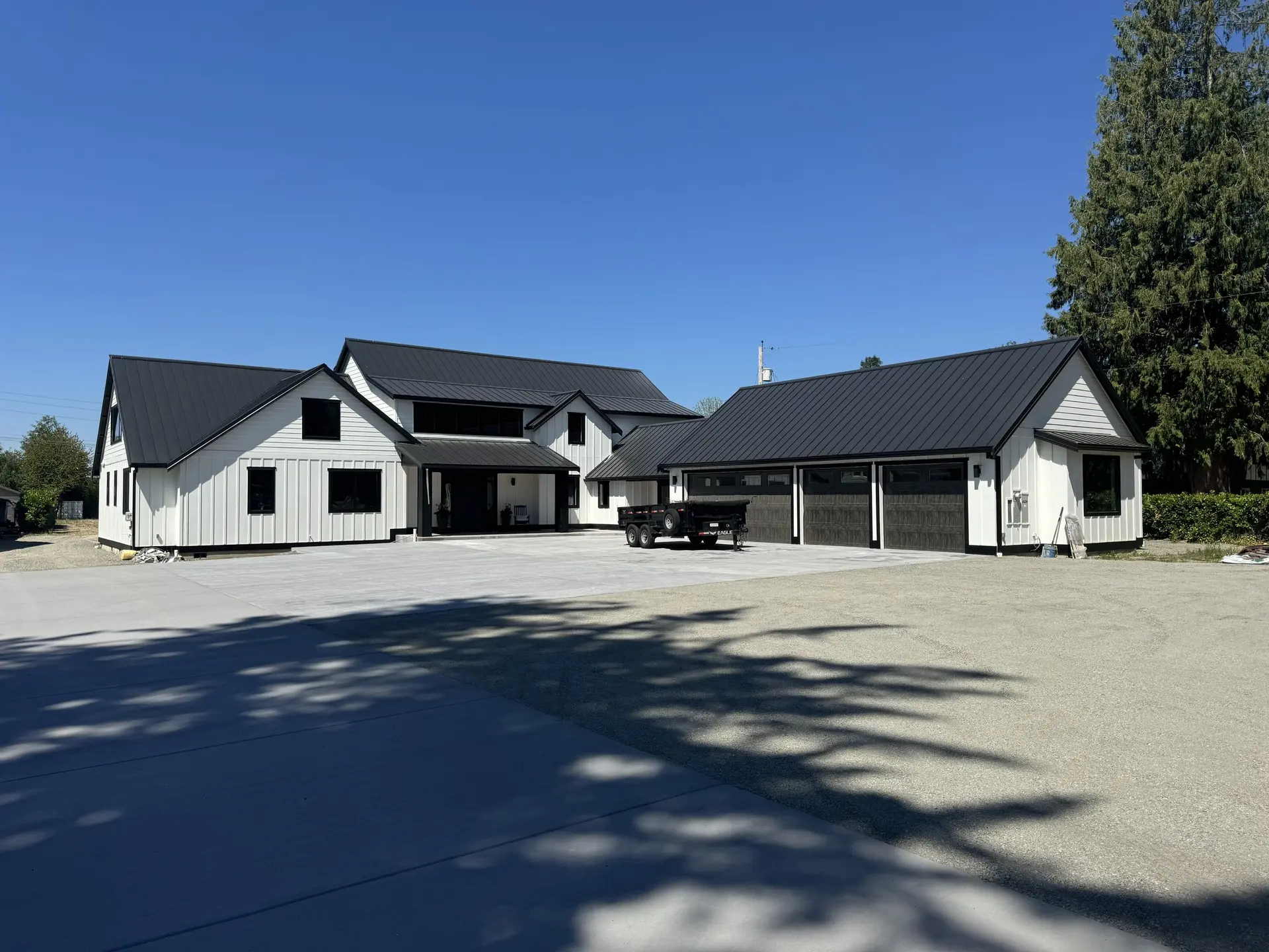 A modern farmhouse in white board-and-batten under a black standing-seam roof, with a detached three-bay garage