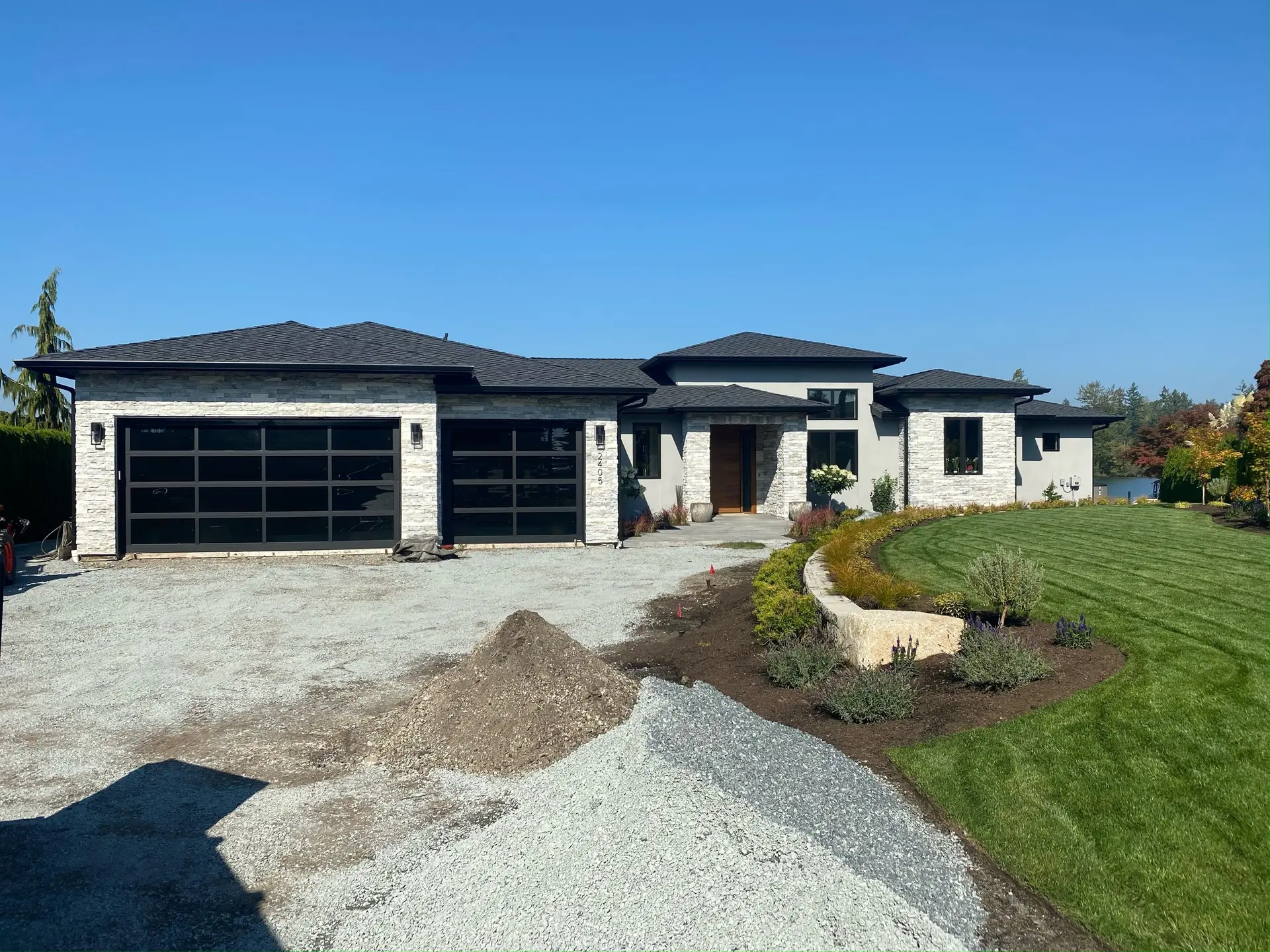 Finished front elevation in stacked stone and stucco with black glazed garage doors and new planting beds