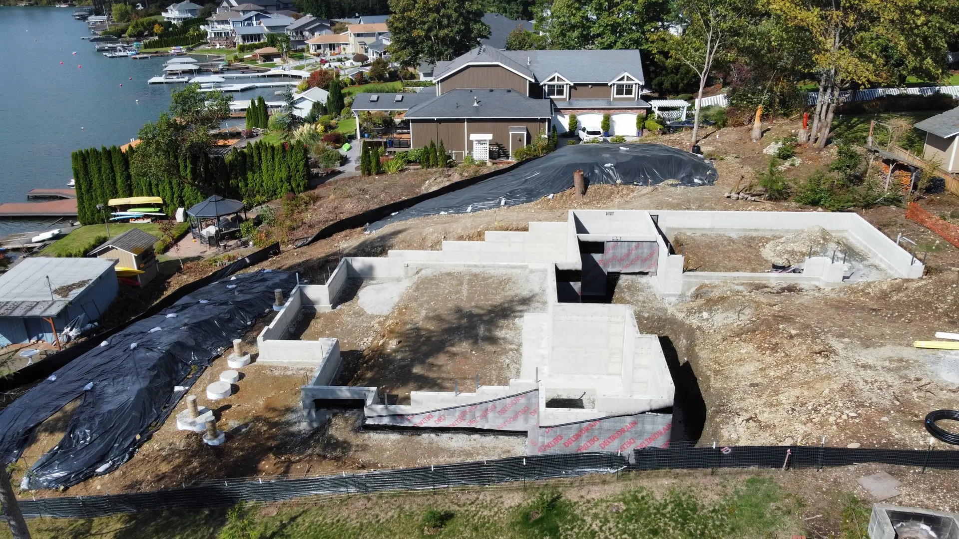Aerial view of poured foundation walls stepping down a lakefront lot, drainage board and silt fence in place