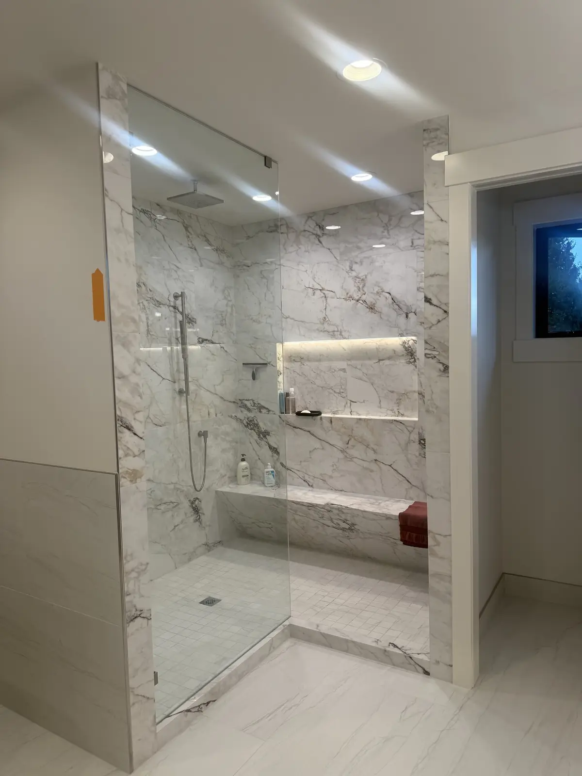 Walk-in shower in book-matched marble with a lit niche and a full-width bench