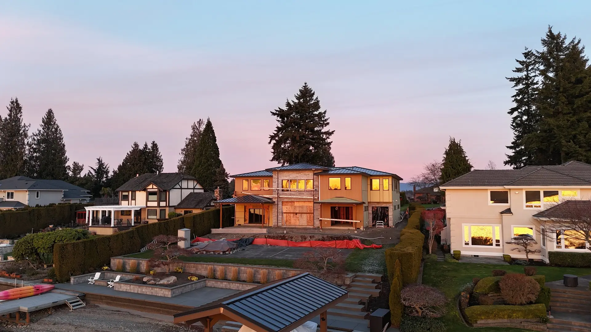 The two-storey house at dusk during construction, windows in and lit from within, sheathing still exposed