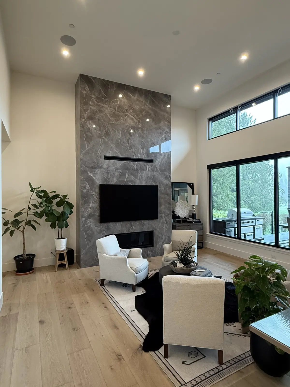 Double-height great room with a full-height stone fireplace and black-framed windows to the fairway