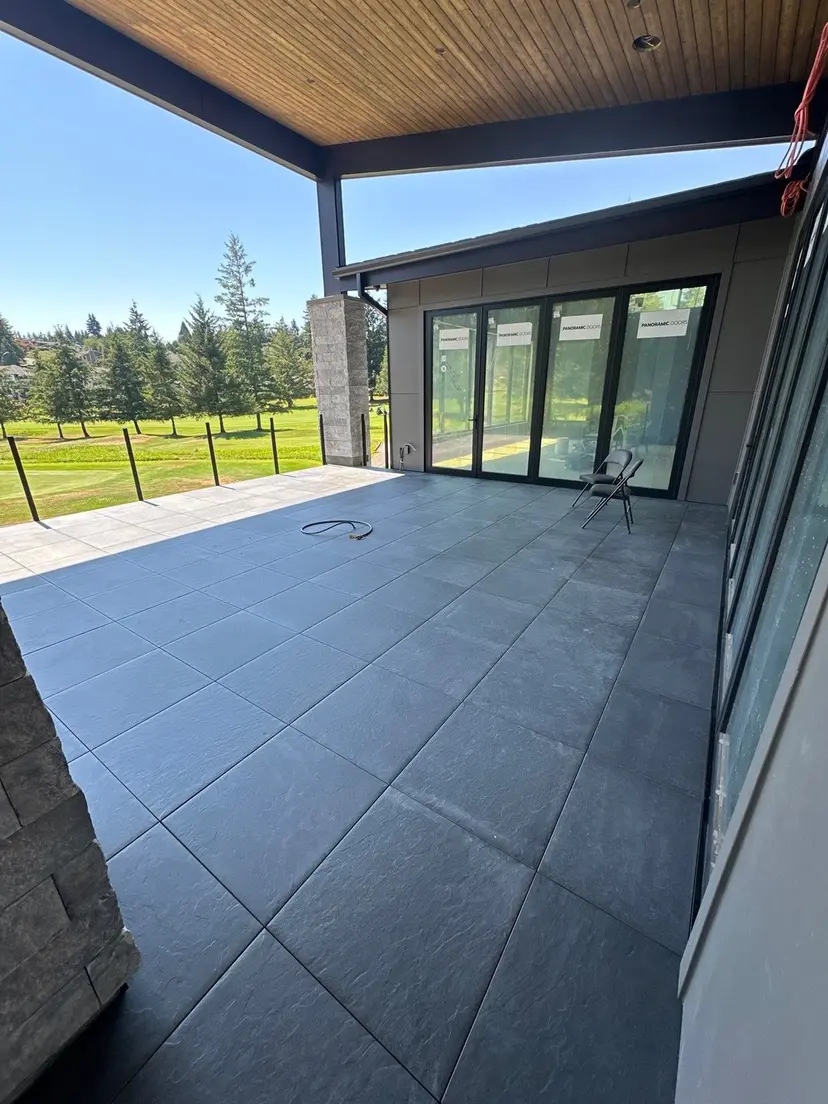 Covered patio in large-format slate under a cedar soffit, panoramic doors folding back to the fairway