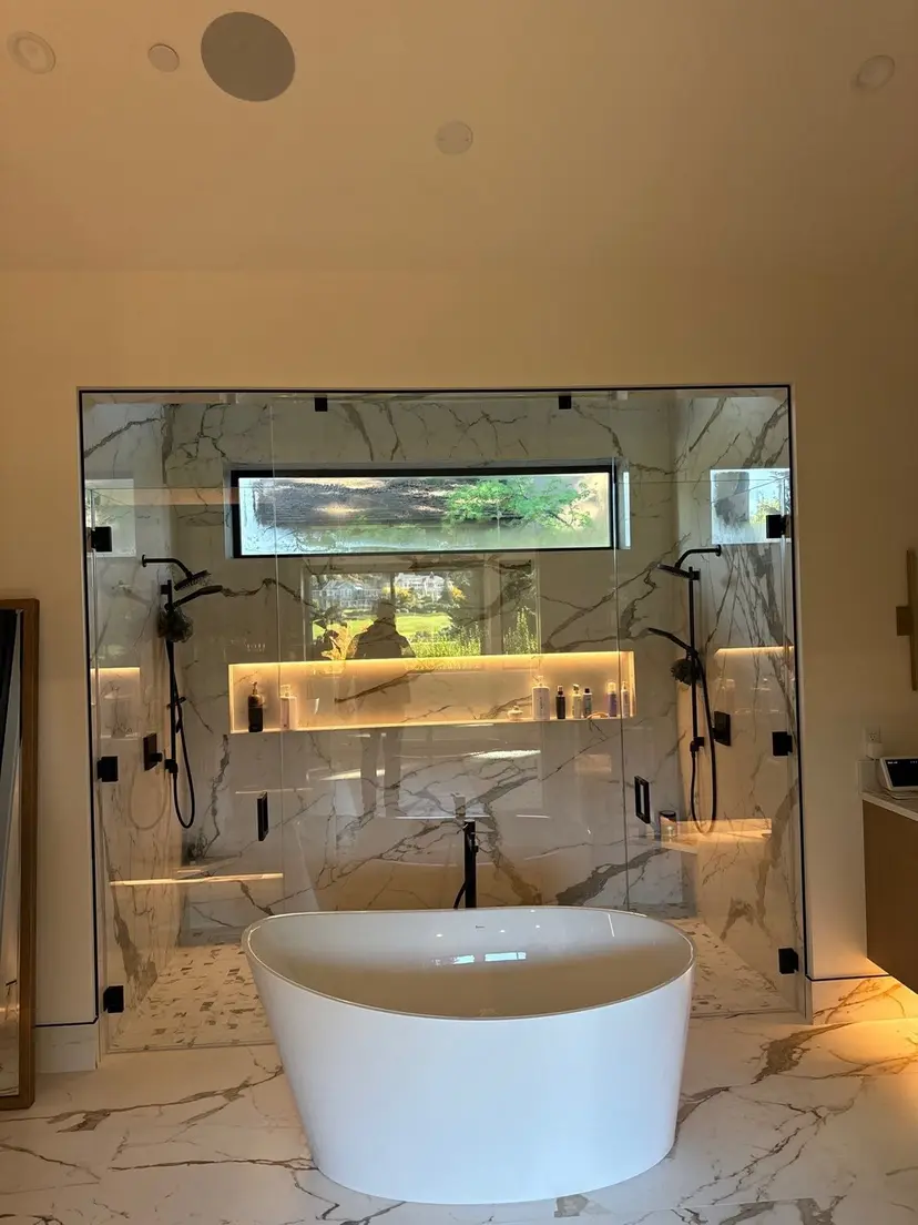 Primary bath in book-matched marble with a glass-walled double shower, lit niche and freestanding tub